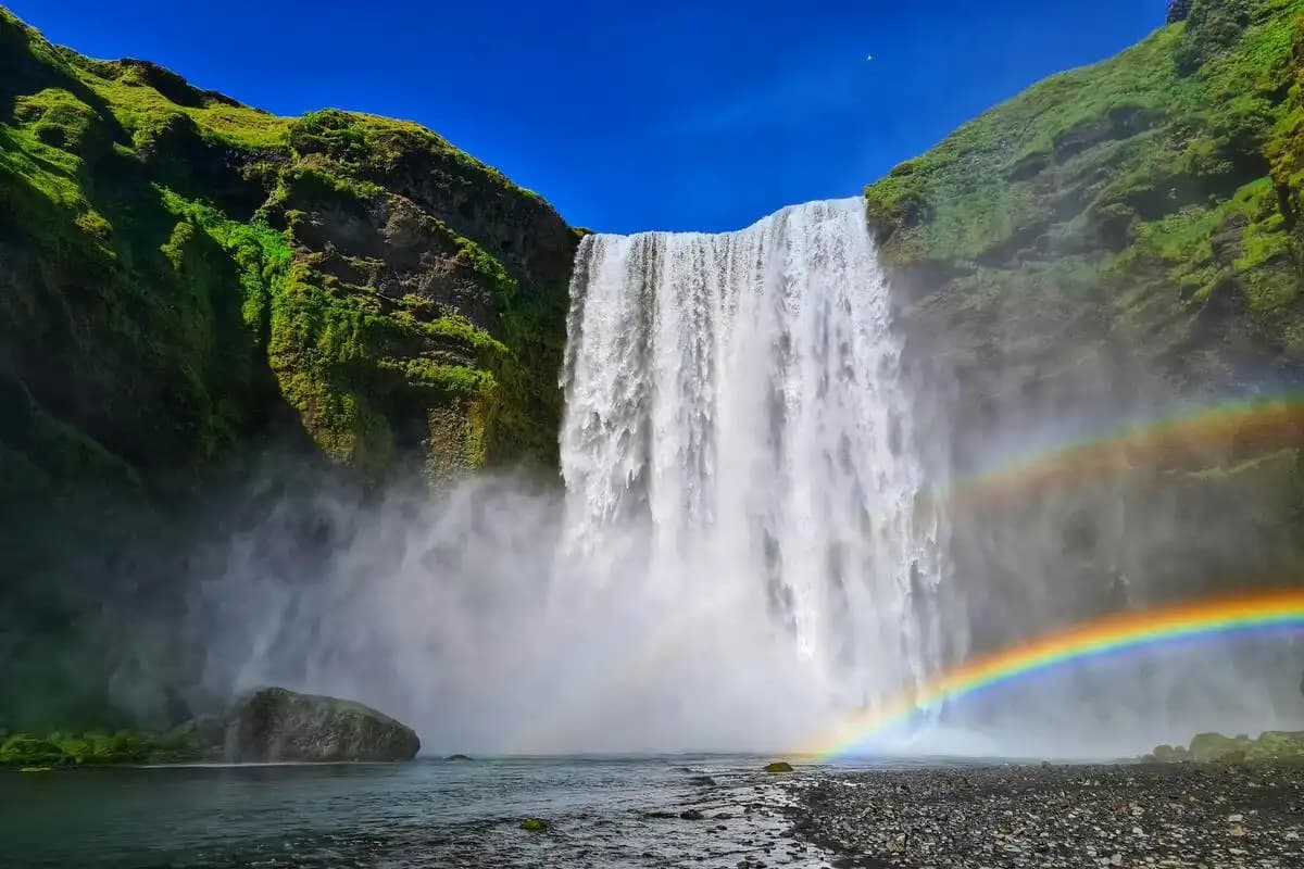 Beautiful-waterfall-with-rainbow-and-green-mountains-under-clear-blue-sky