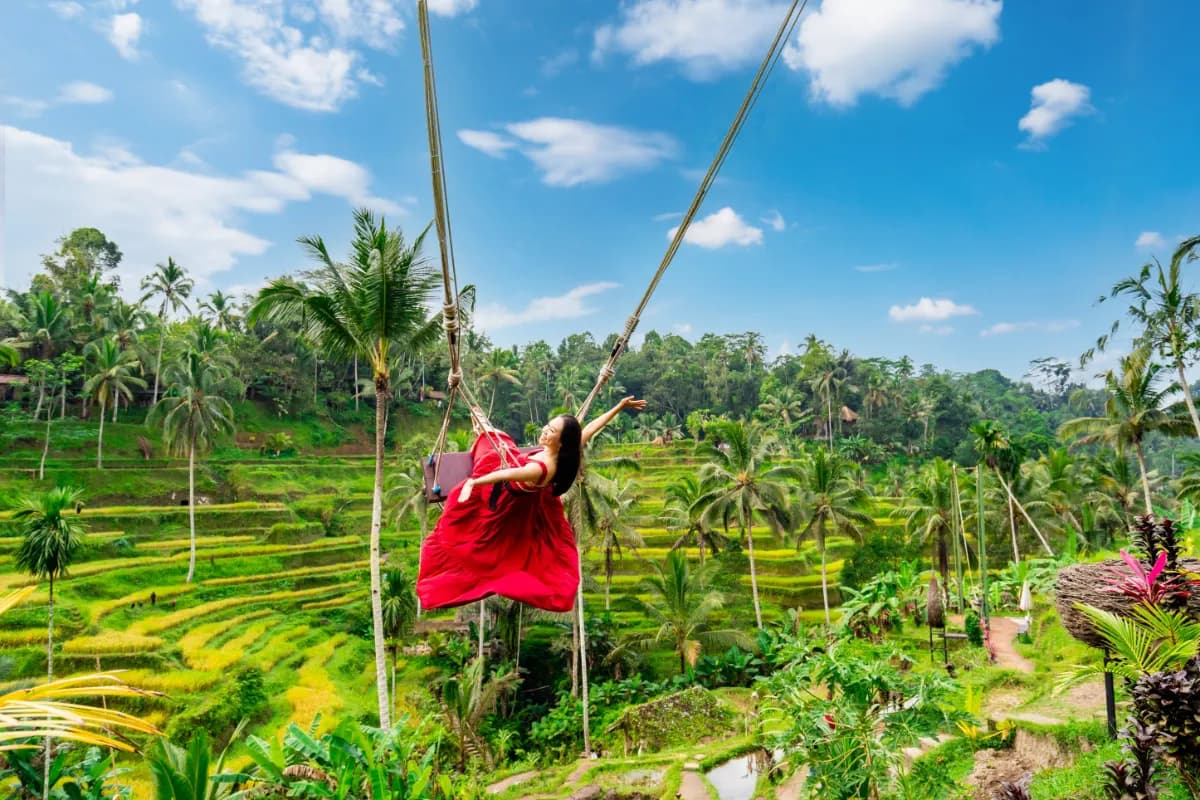 Happy young female tourist in red dress enjoying the Bali swing at tegalalang rice terrace in Bali