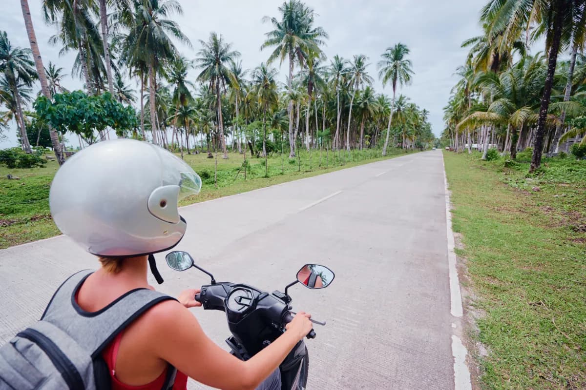 Woman in helmet riding scooter on the road with palm trees in Bali
