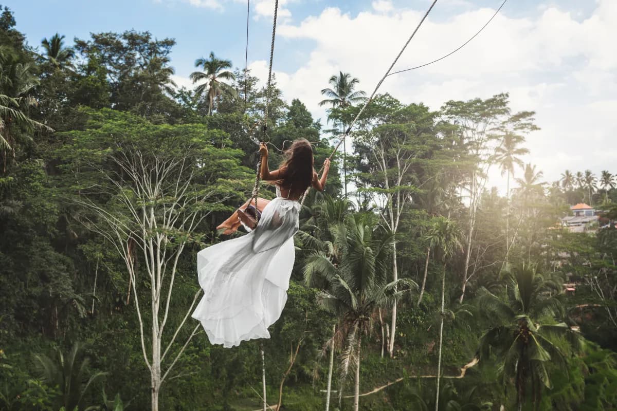 Young woman wearing white dress swinging on rope swings with beautiful view on rice terraces.