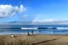 People standing on the beach and many surfers riding long boards