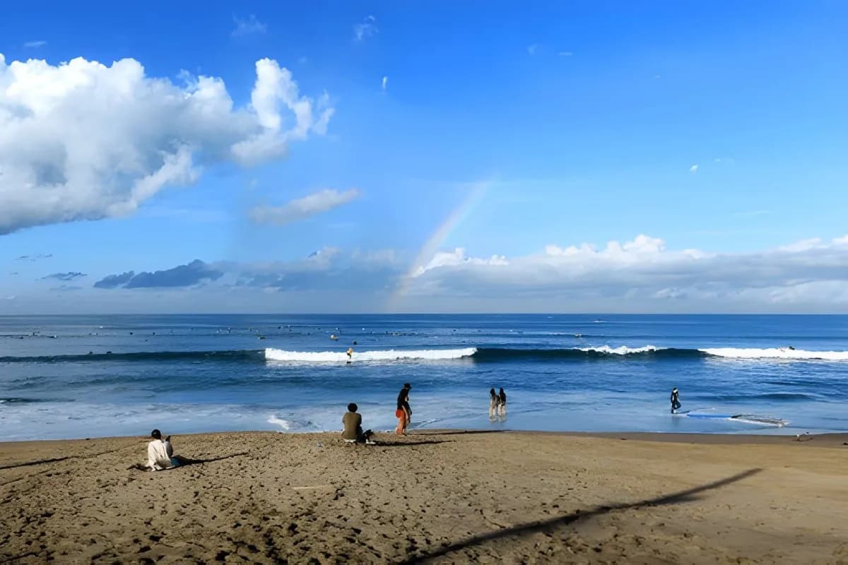 People standing on the beach and many surfers riding long boards